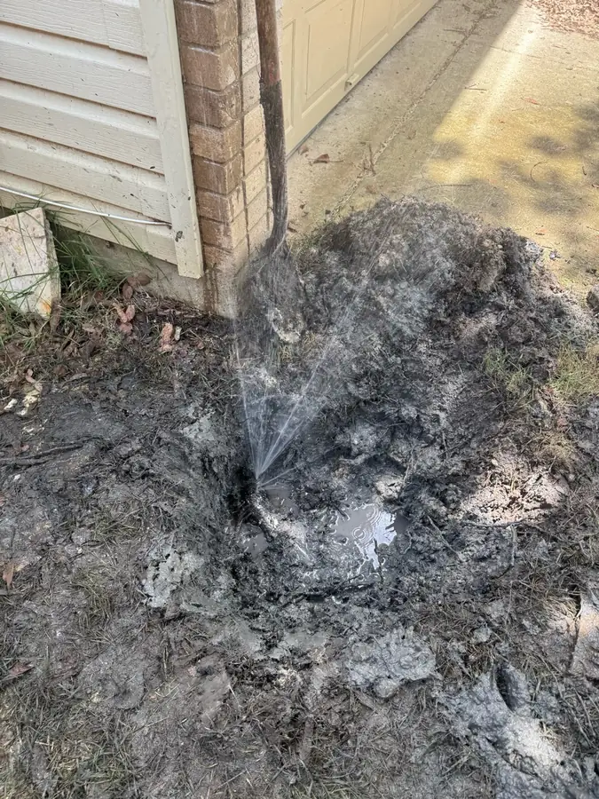 Water spraying from a broken line beside a house before Rapid Plumbing repair